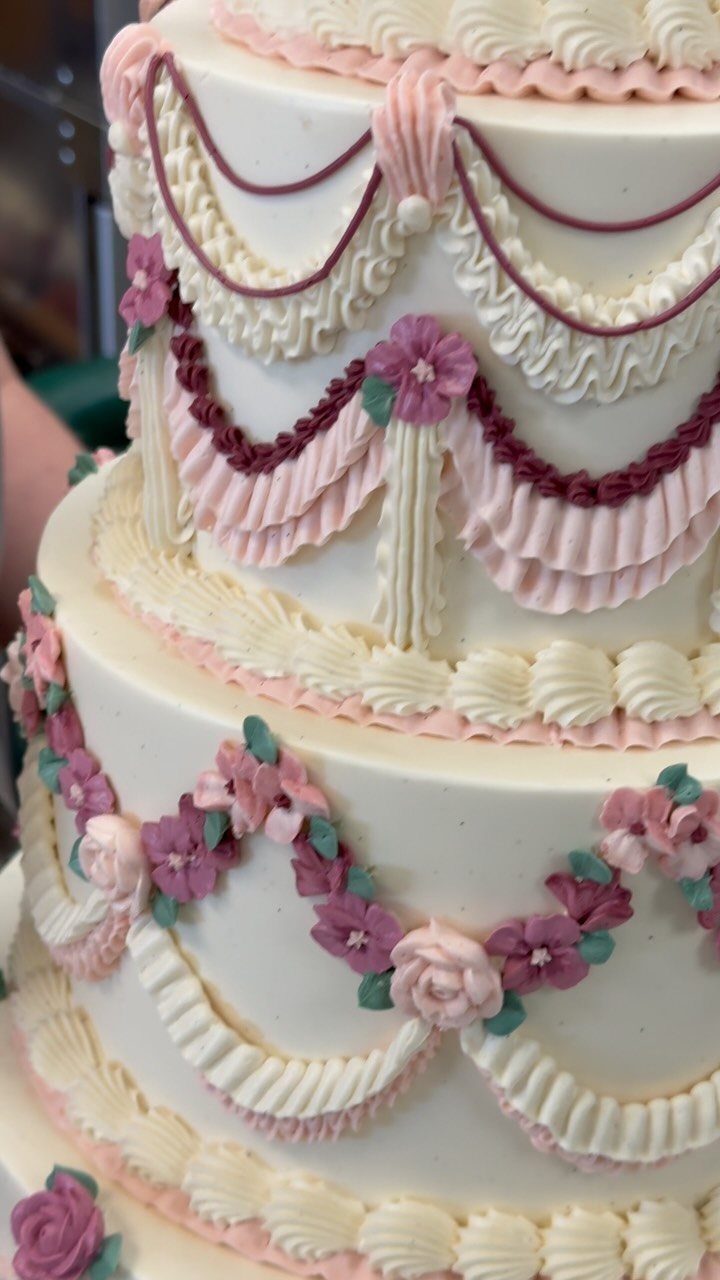 Multi-tiered white cake decorated with pink and purple buttercream flowers and piped swags.