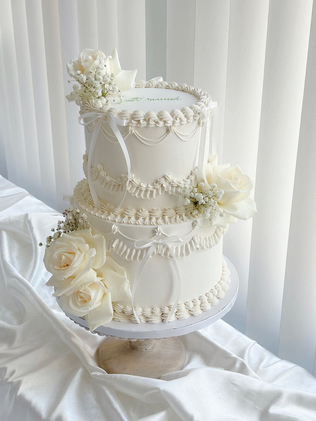 Two-tier white wedding cake decorated with white roses and delicate buttercream piping.