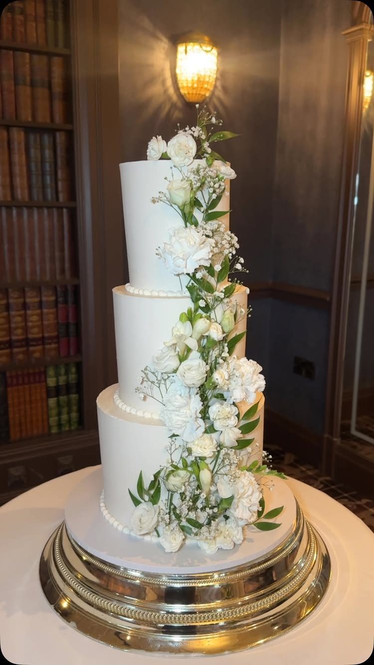 Three-tiered white wedding cake with white flowers cascading down the side on silver stand