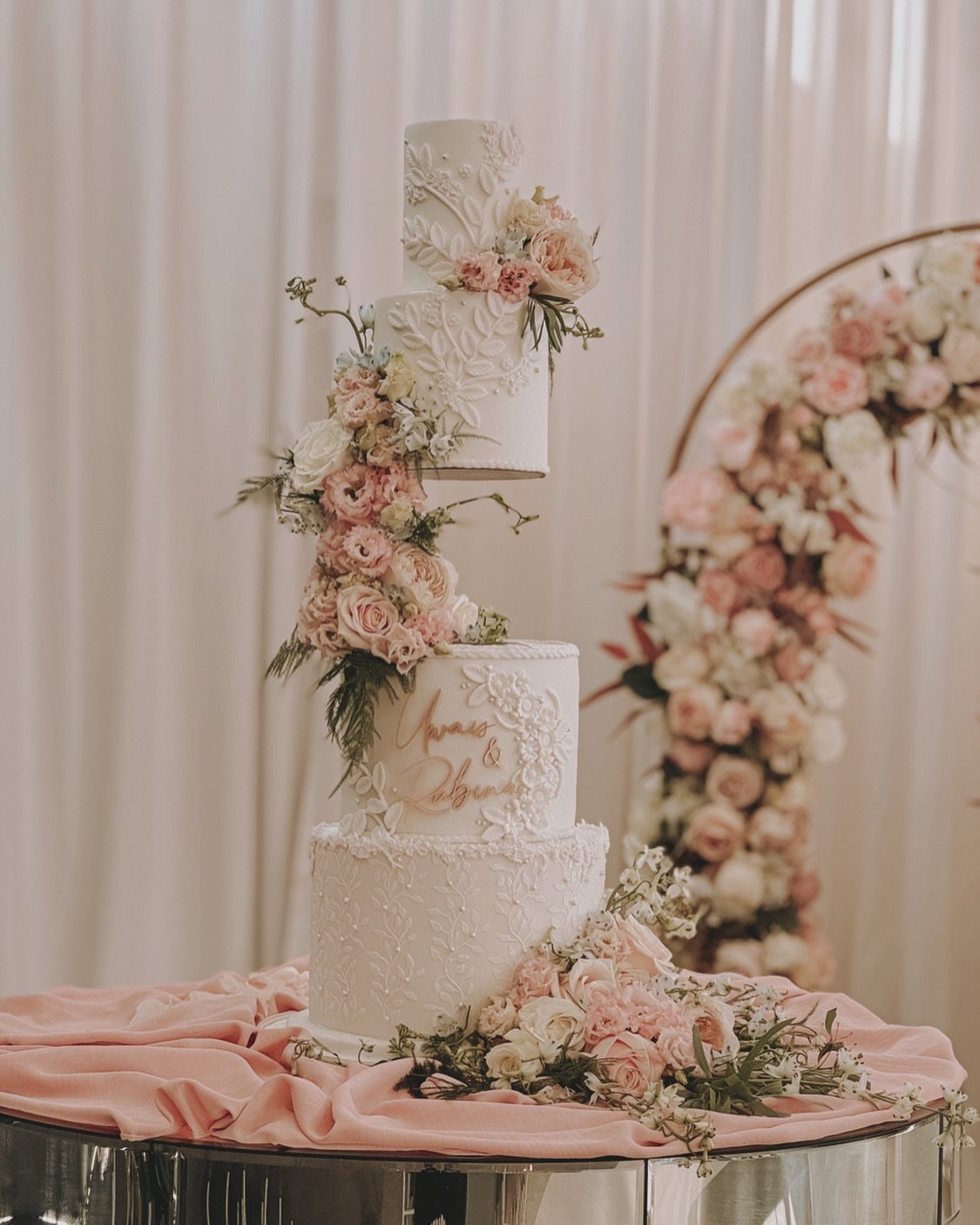Multi-tiered white wedding cake adorned with pink and white roses and lace textures.