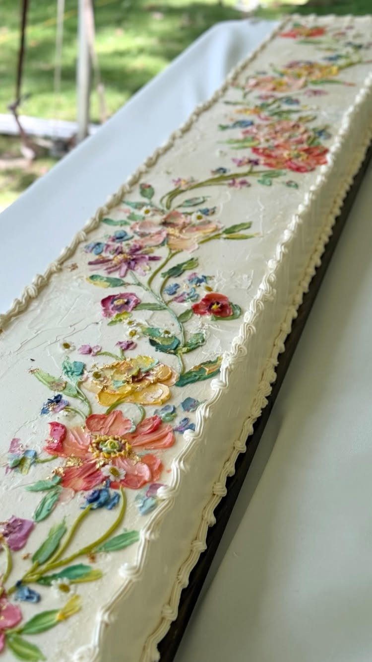 Rectangular white cake decorated with colorful painted floral designs and buttercream borders.