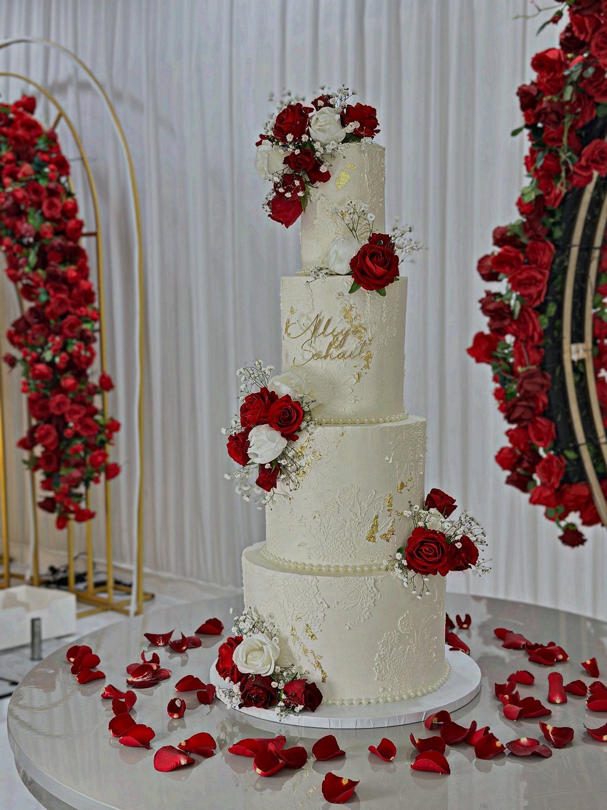 Four-tier white wedding cake adorned with red and white roses and baby's breath.