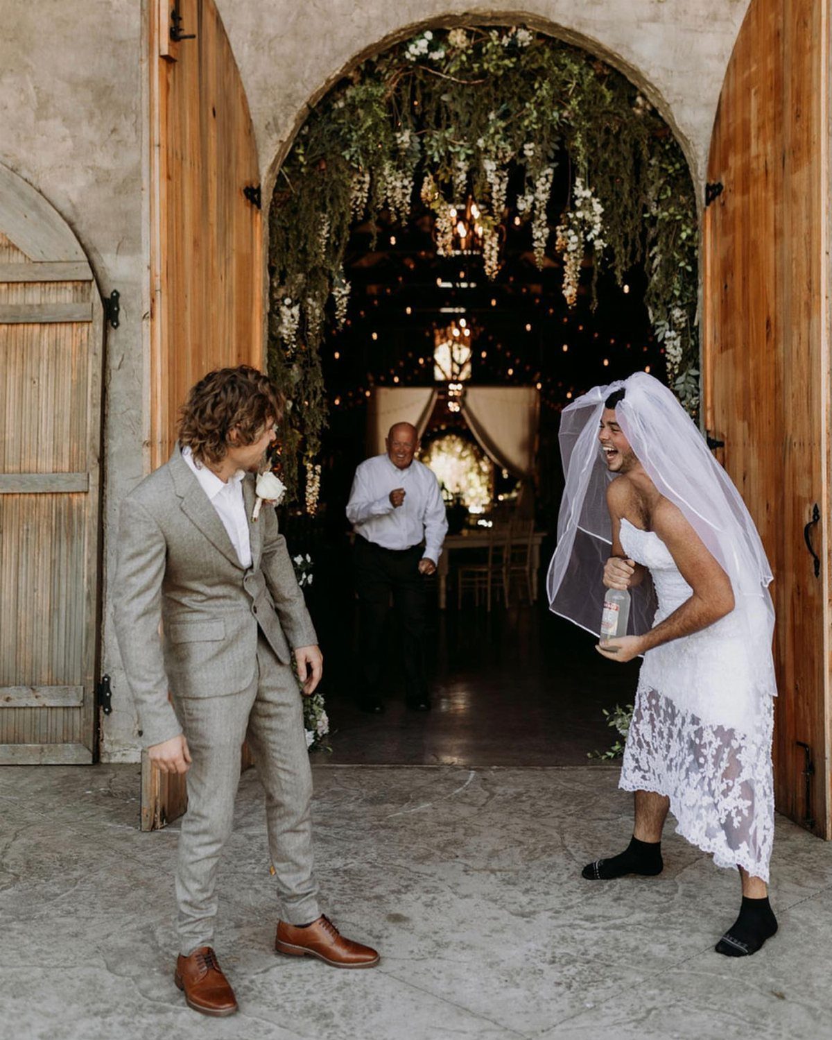 Two men laughing during a first look, one wearing a wedding dress and veil.