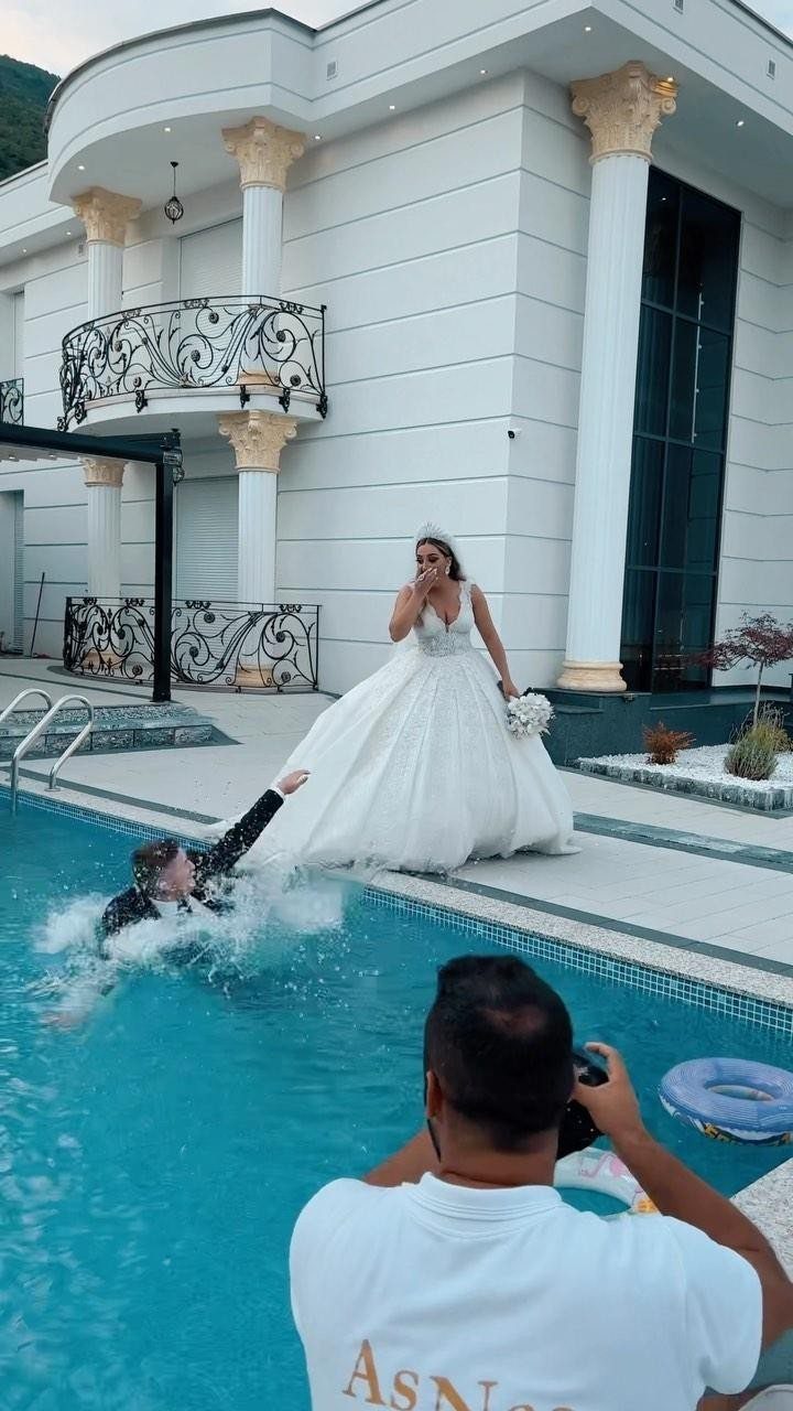 Bride watching groom fall into a swimming pool during a wedding photo shoot