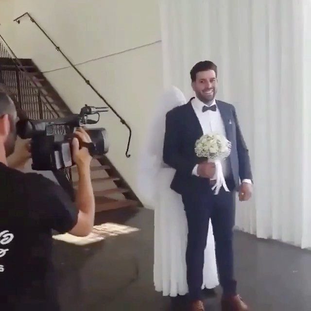 Groom holding a bridal bouquet while a bride hides behind him during filming.