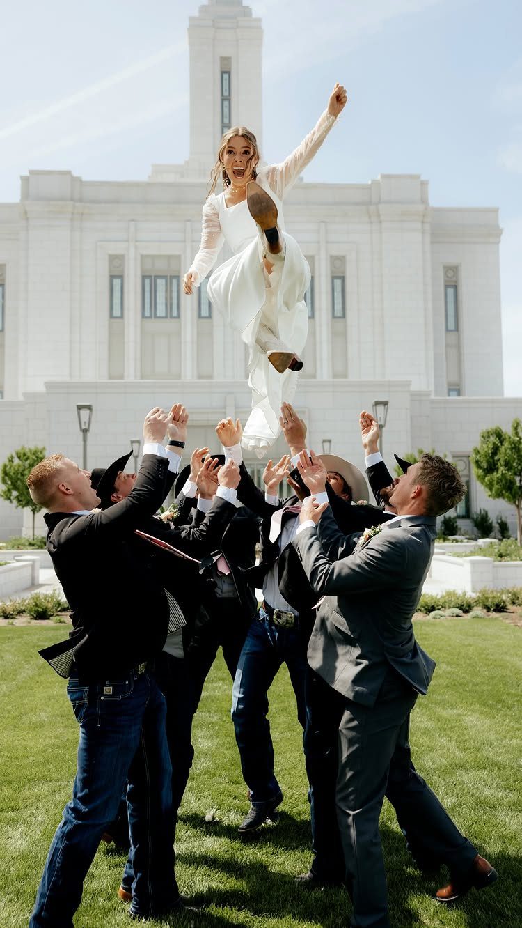 Bride in white dress tossed in the air by men in suits outdoors