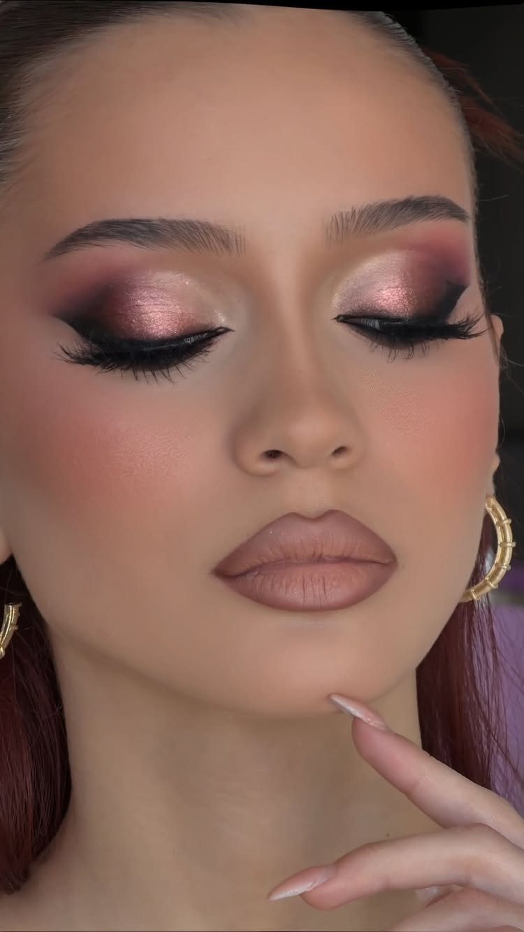 Woman with glamorous rose-gold eyeshadow, winged eyeliner, and matte mauve lipstick.