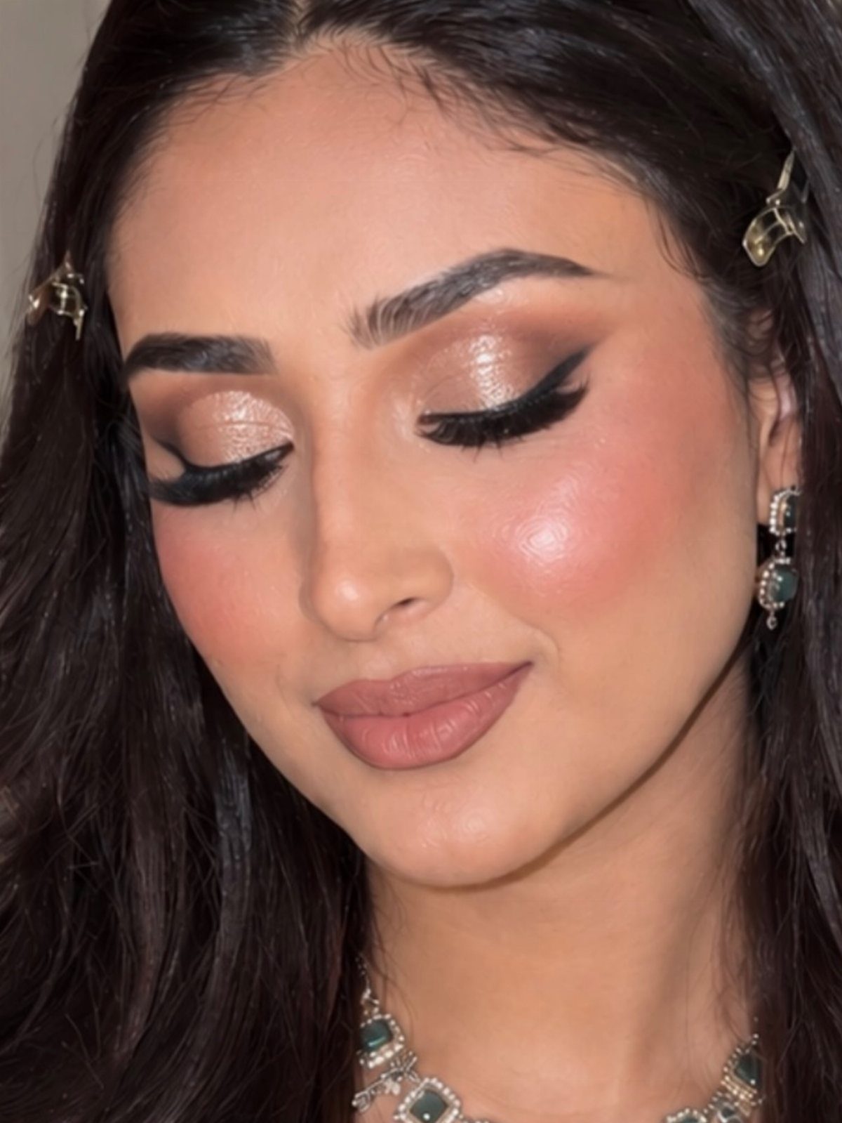 Woman with shimmering gold eyeshadow, long lashes, and nude lips wearing bridal jewelry.