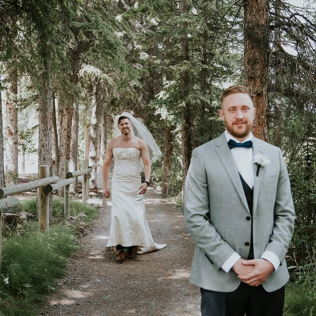 Man in grey suit with a muscular man in wedding dress behind him