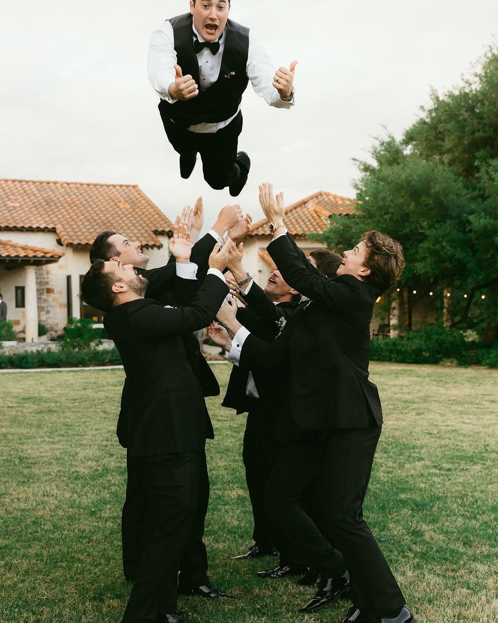 Groom being tossed into the air by groomsmen on a green lawn
