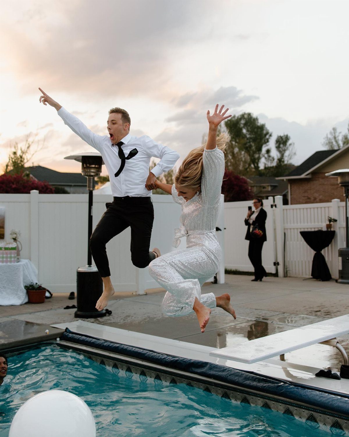 Couple in wedding attire jumping off a diving board into a swimming pool.