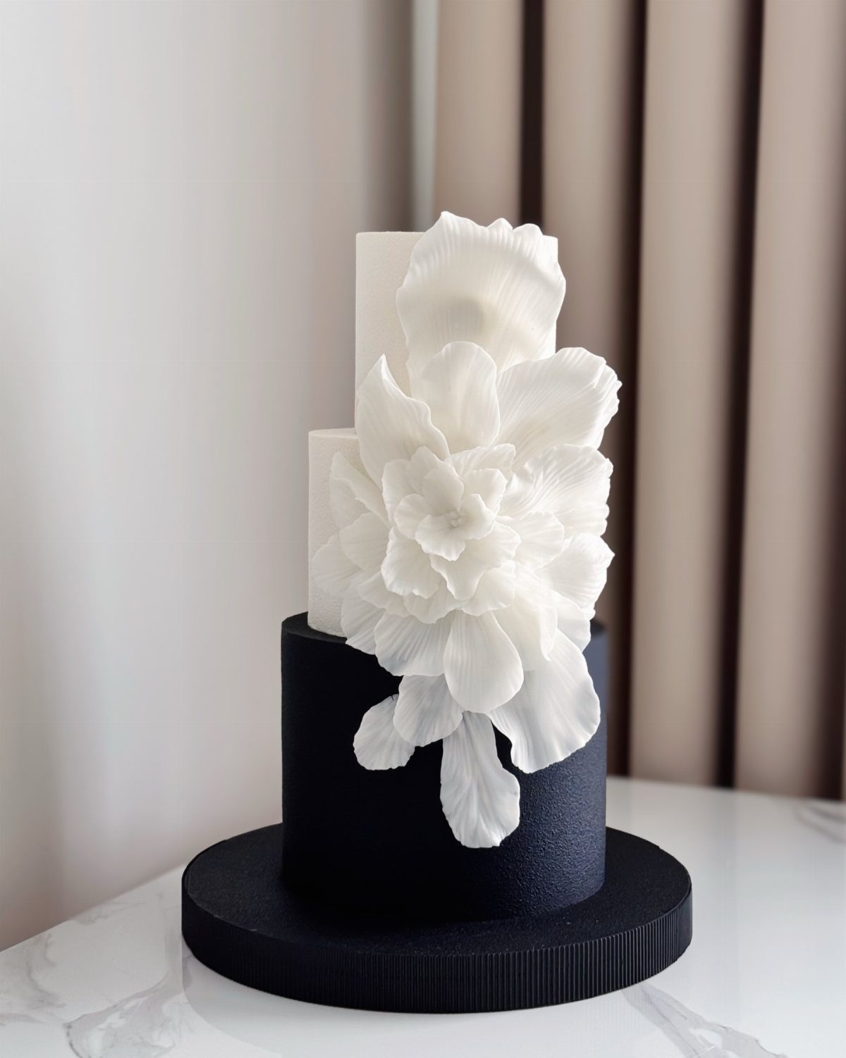 Three-tiered cake with black and white layers and a large white sugar flower.