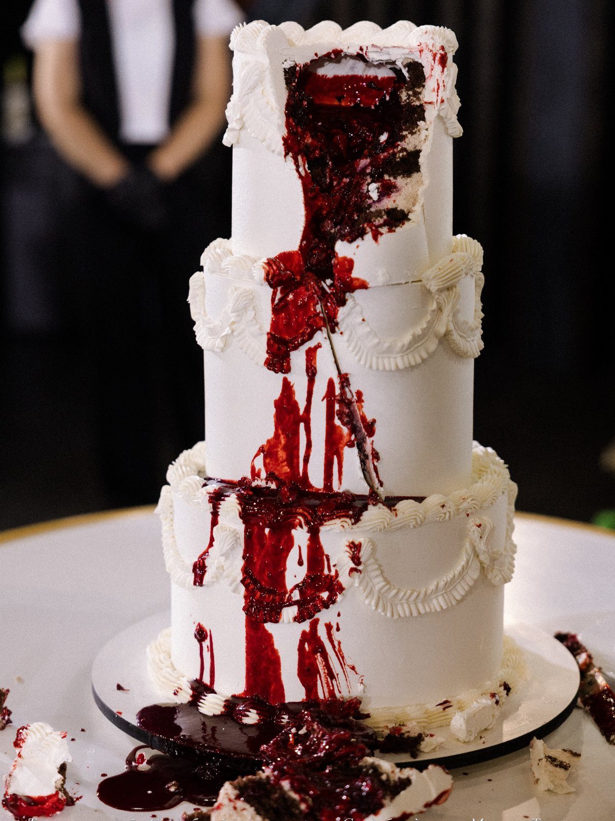 Three-tier white wedding cake with red syrup dripping like blood from a gash