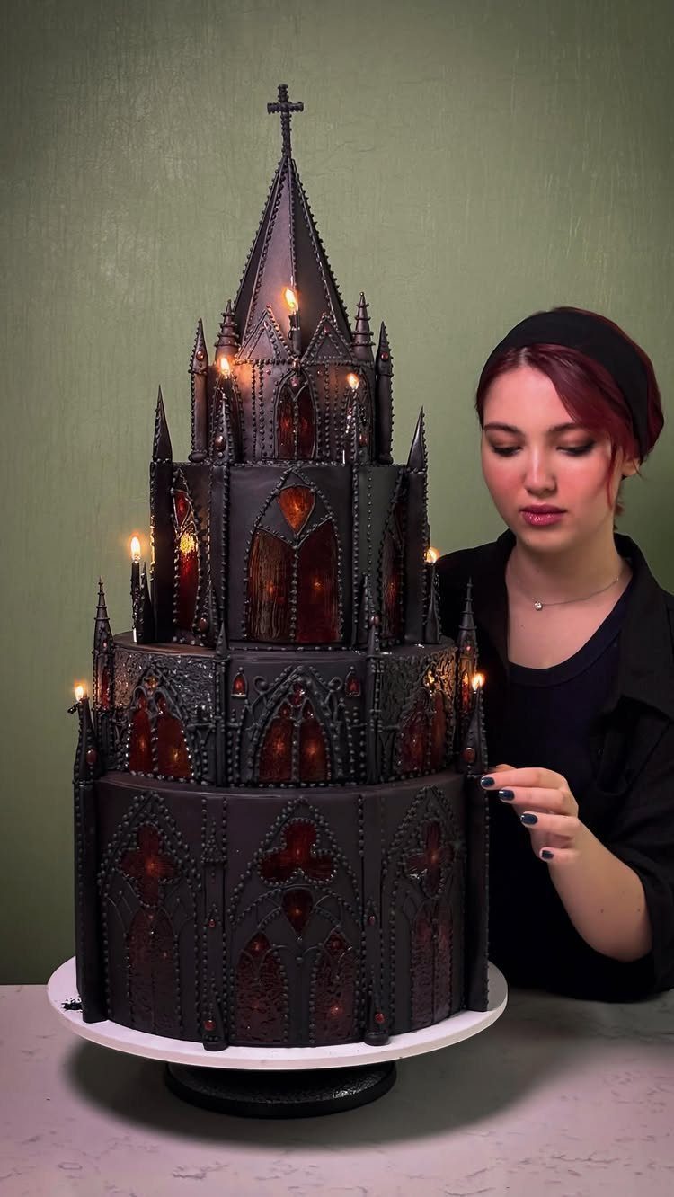 Gothic cathedral cake in black with glowing orange windows and a woman beside it
