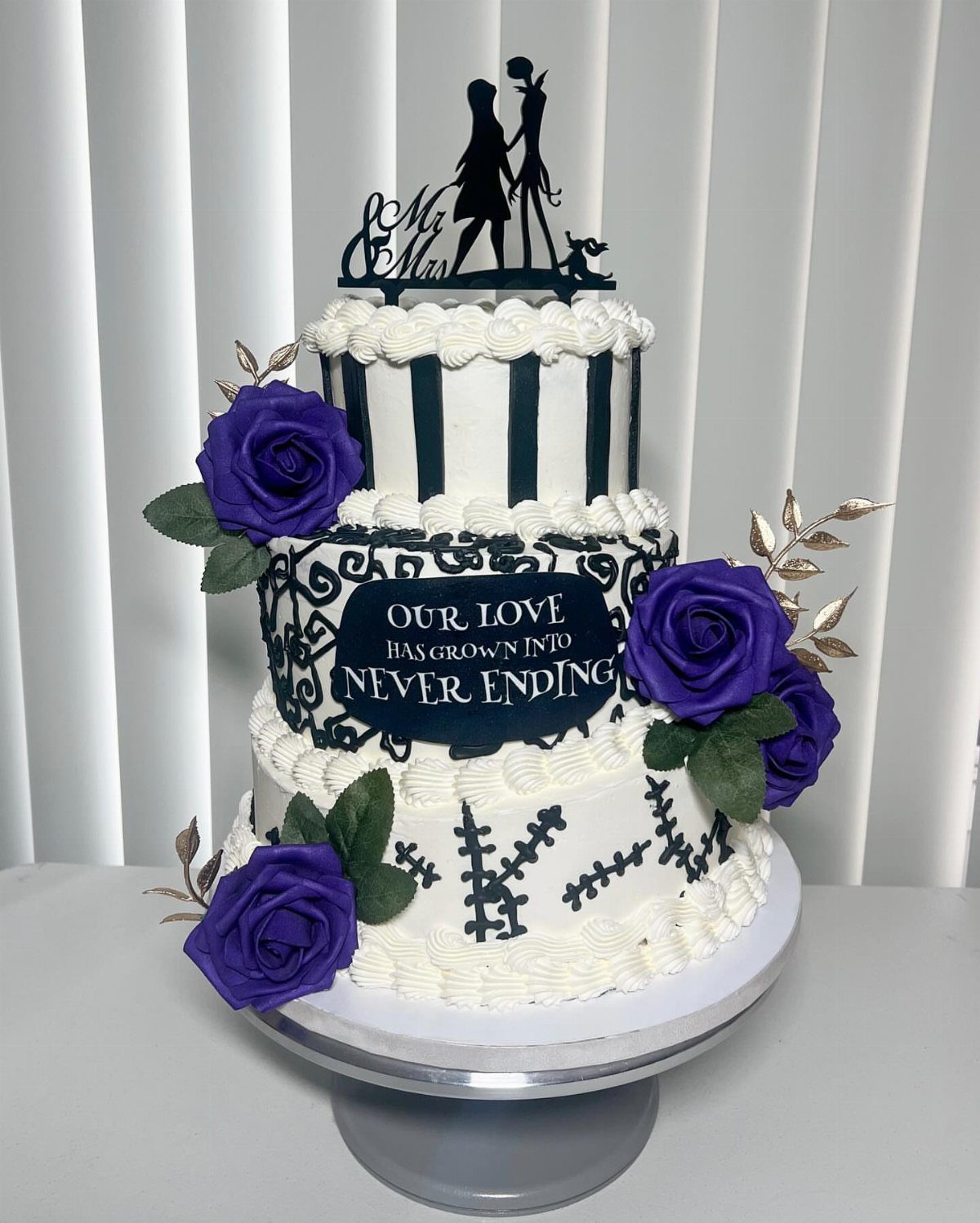 Three-tier white wedding cake with purple roses and Nightmare Before Christmas inspired decorations.
