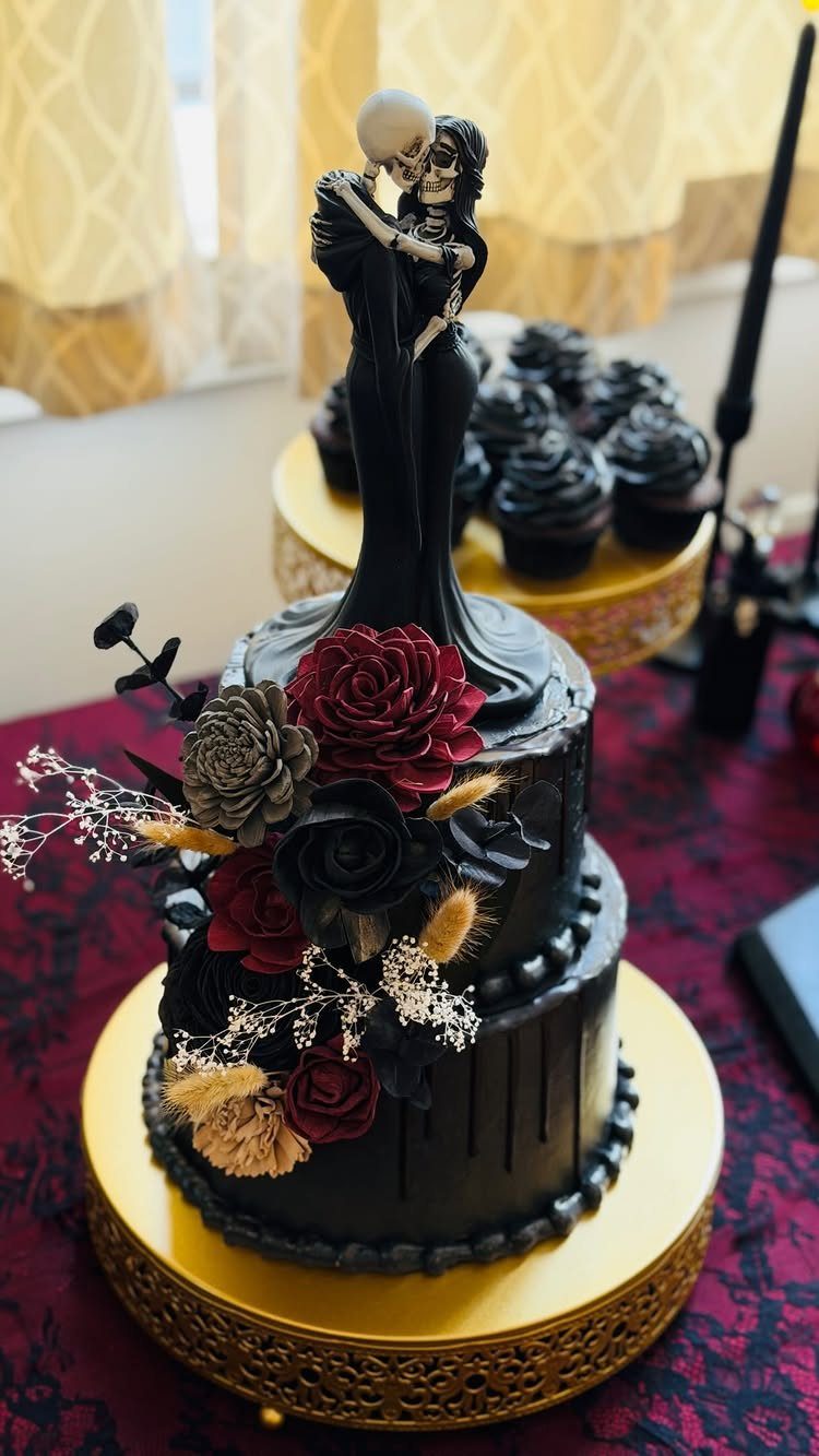 Two-tier black wedding cake with red roses and skeletal couple cake topper.