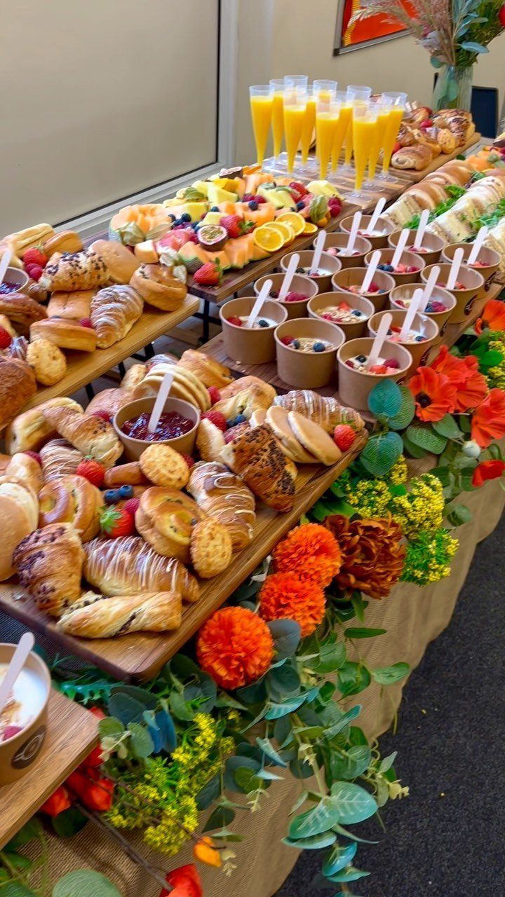 Breakfast grazing table with pastries, fresh fruit, orange juice, and colorful floral decorations.