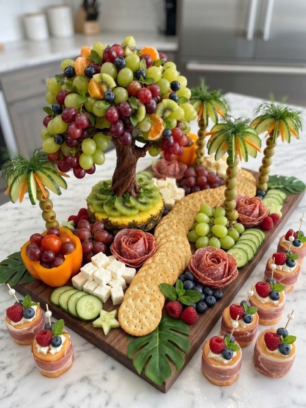 Tropical themed grazing board with fruit tree, cheese, cured meats, and crackers.