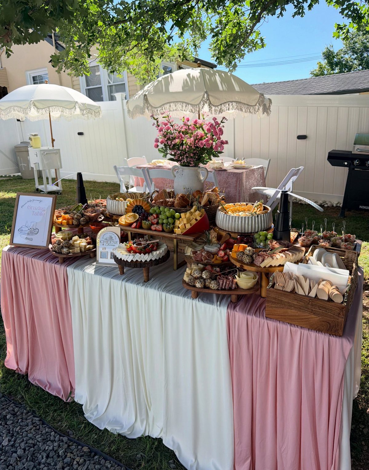 Grazing table with food labels, cured meats, cheeses, and fruits on draped linens.