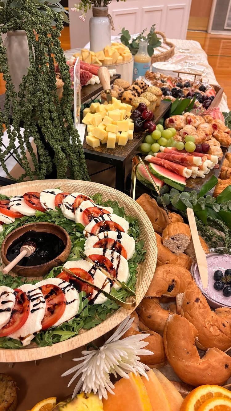 Grazing table with caprese salad, bagels, and cheeses on a raised wooden stand.