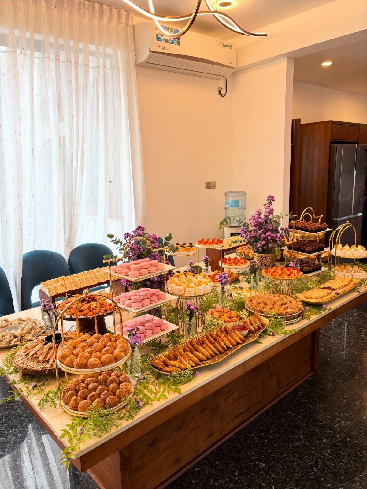 Grazing table with assorted pastries and desserts decorated with green vines and purple flowers.
