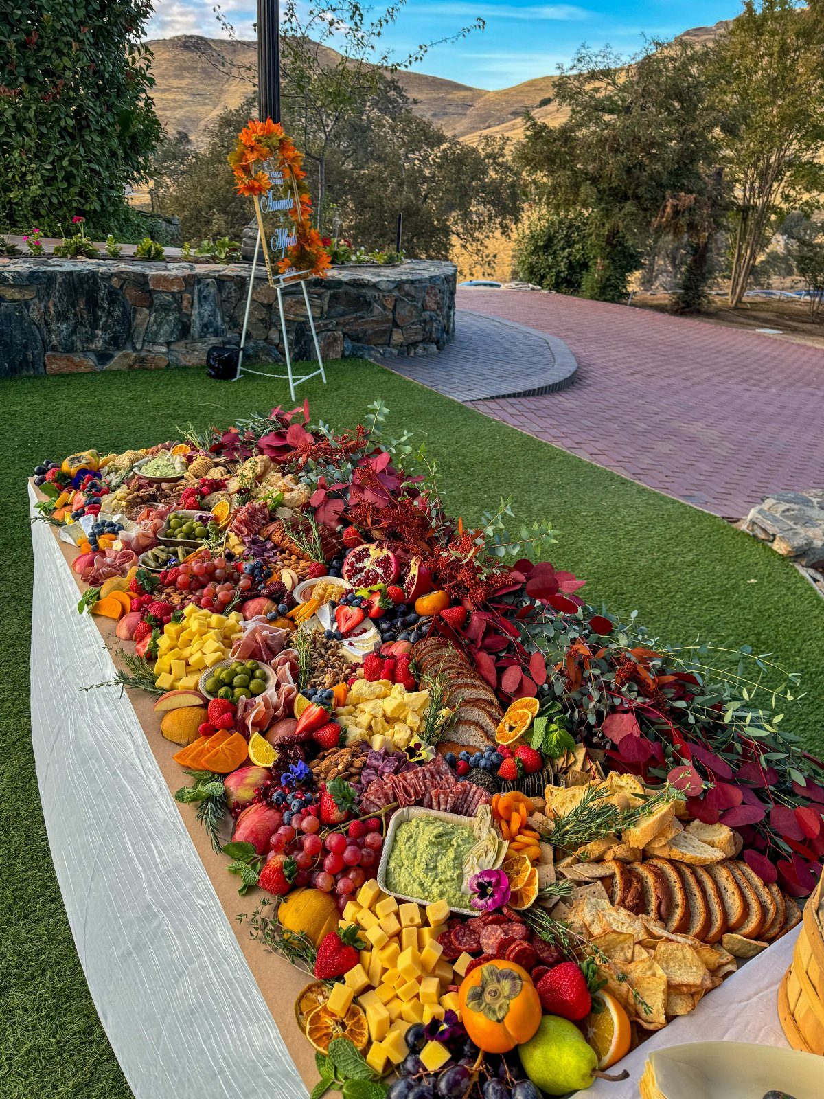 Lavish grazing table with diverse cheeses, fruits, and meats decorated with autumn leaves.