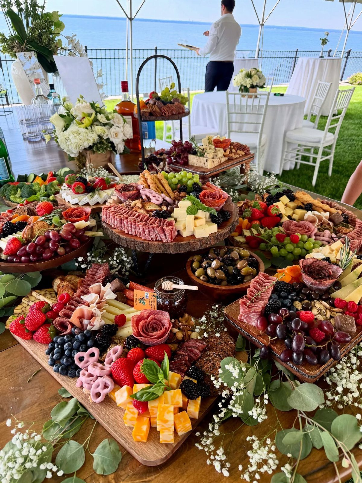 Wooden boards and platters filled with meats, cheeses, and fruits on a grazing table.
