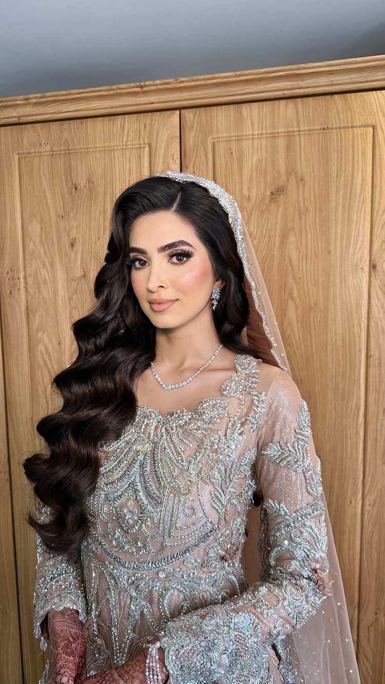 Woman with voluminous dark brown waves wearing an embellished silver bridal gown and veil.