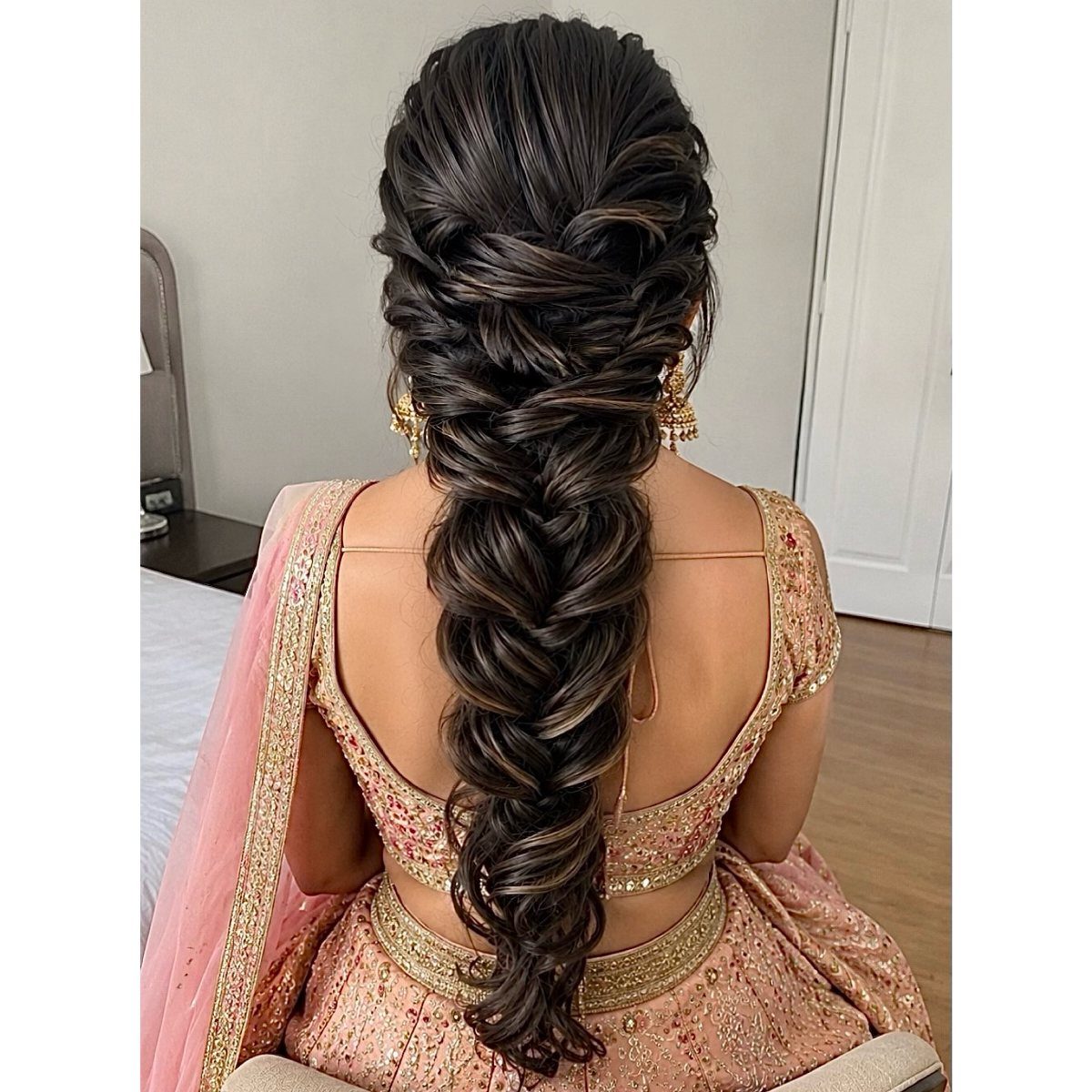 Intricate voluminous bridal braid on a woman wearing a pink and gold lehenga.