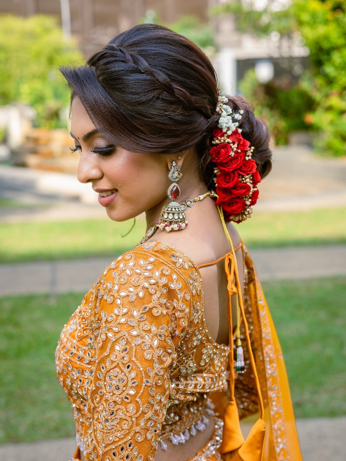 Woman with a low bridal bun adorned with red roses and traditional jewelry