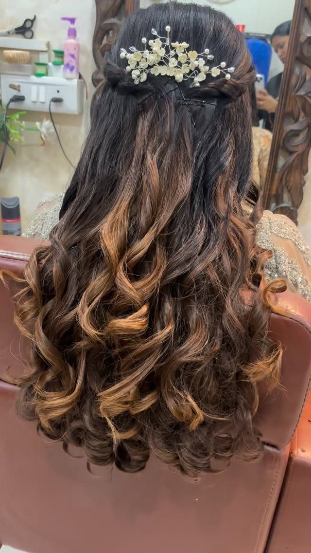 Long curly brown hair with a white floral accessory pinned at the back.