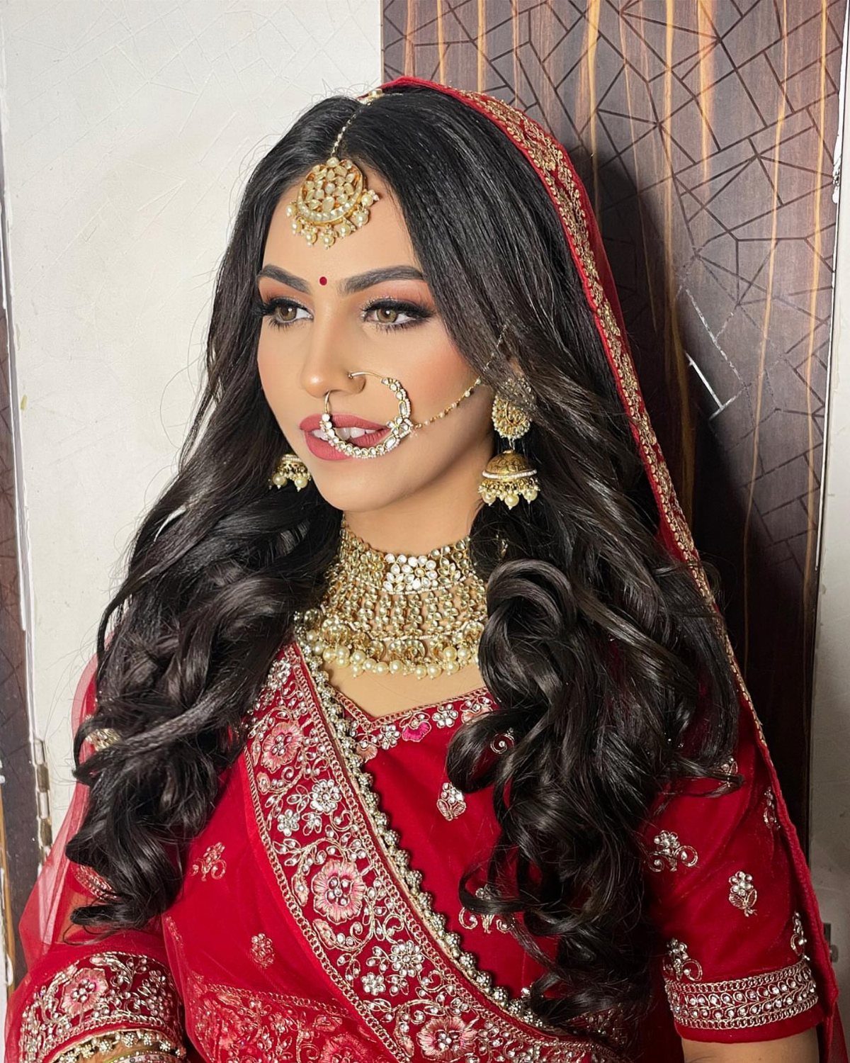 Indian bride with long open wavy hair wearing red bridal attire and gold jewelry