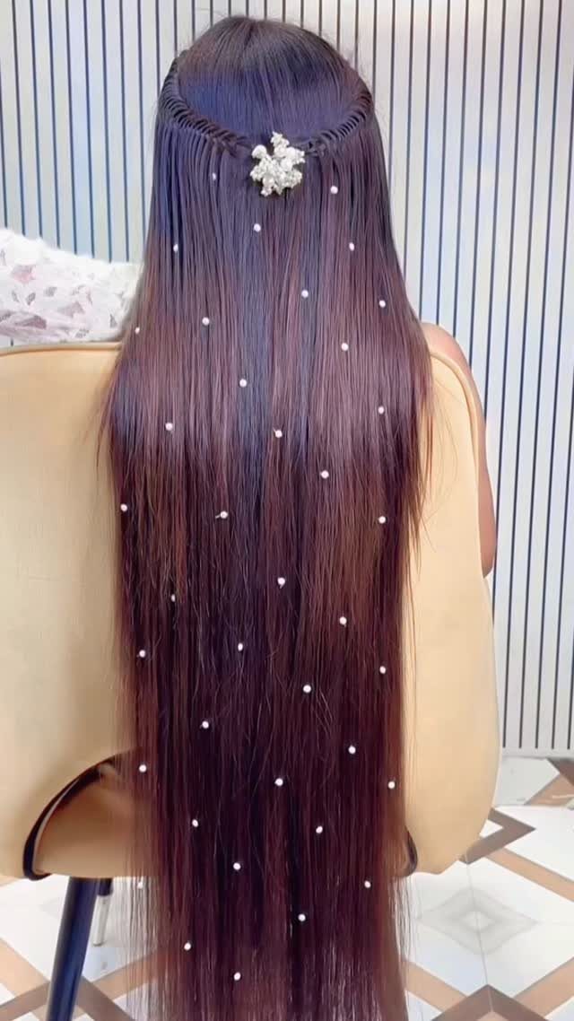 Long straight brown hair with a small braid and scattered white pearl accessories.