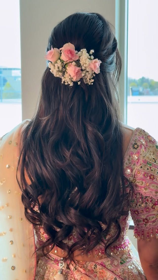 Woman with long wavy hair adorned with pink roses and white baby's breath.