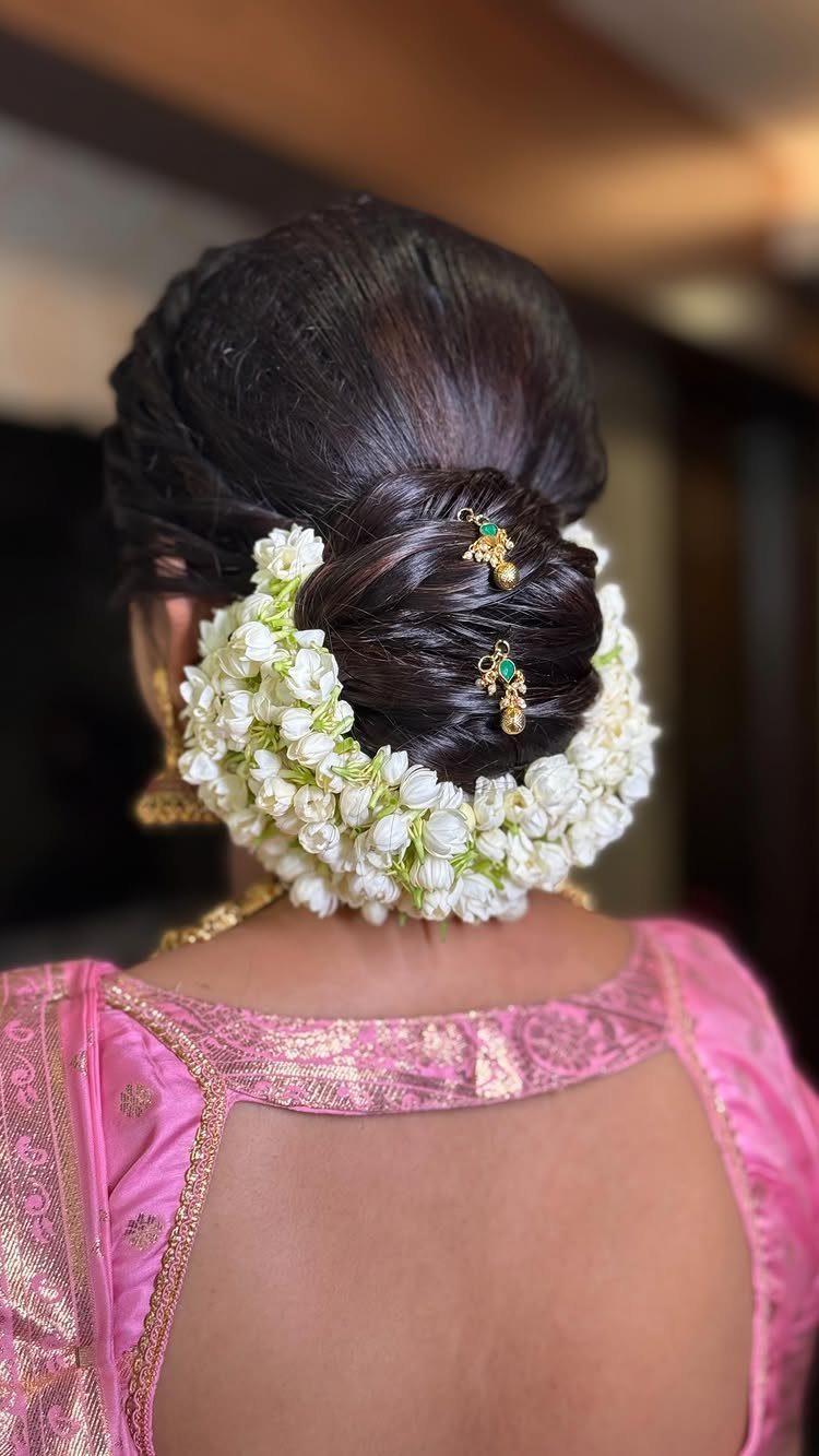 Woman's dark hair in a bridal bun encircled by white jasmine flowers and gold jewelry
