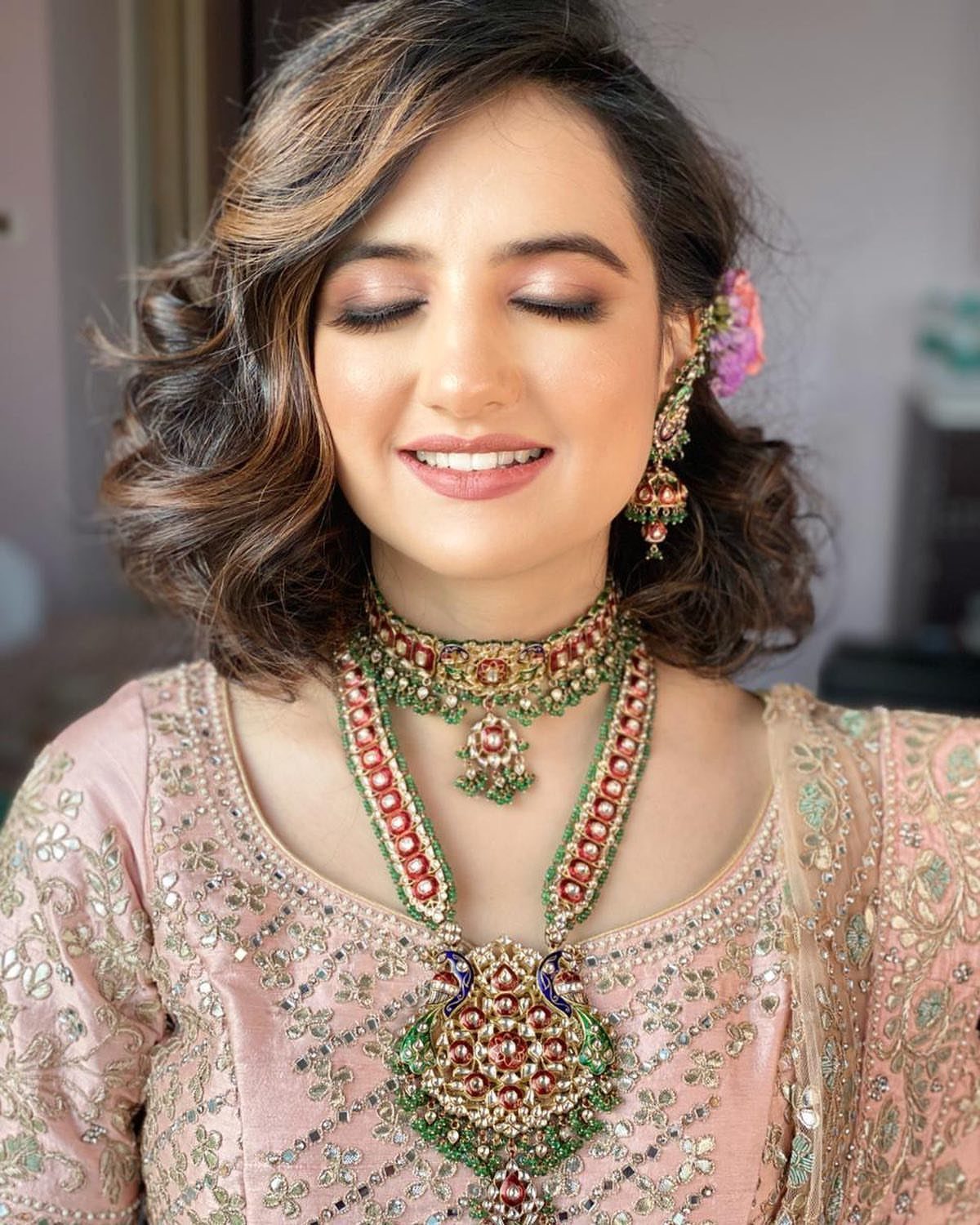 Woman with soft short curls wearing traditional Indian bridal jewelry and pink attire.