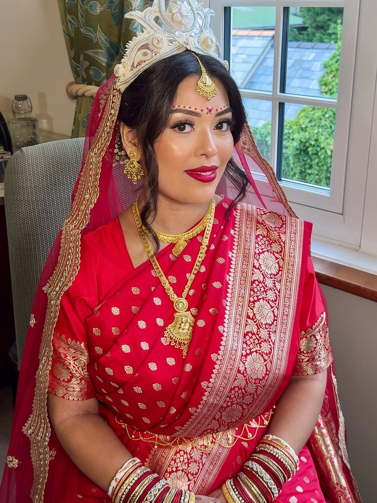 Indian bride wearing a red saree, gold jewelry, and bold red lipstick.