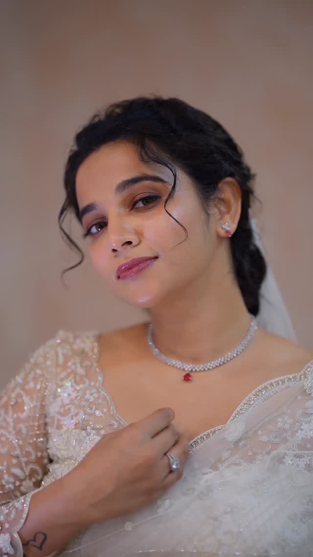 Woman with glowing bridal makeup wearing a white embroidered dress and diamond jewelry.