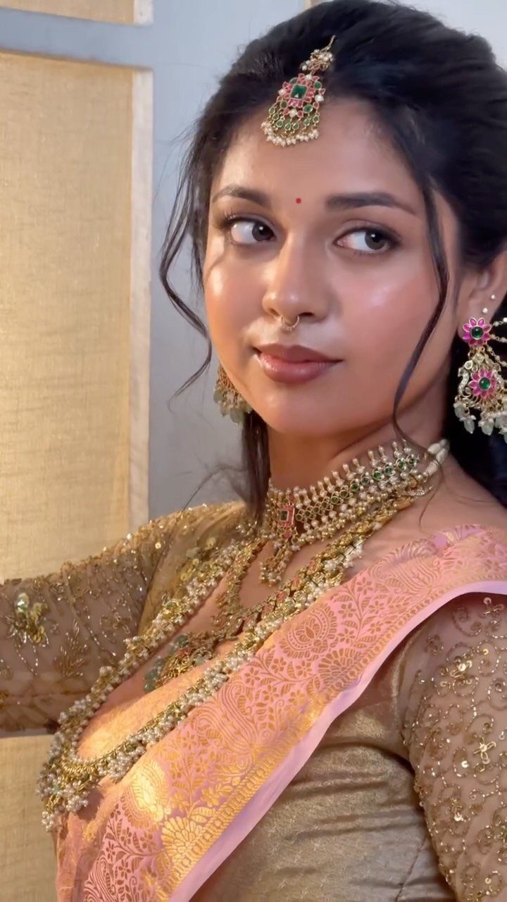 Indian bride with natural makeup wearing gold jewelry and a pink and gold saree