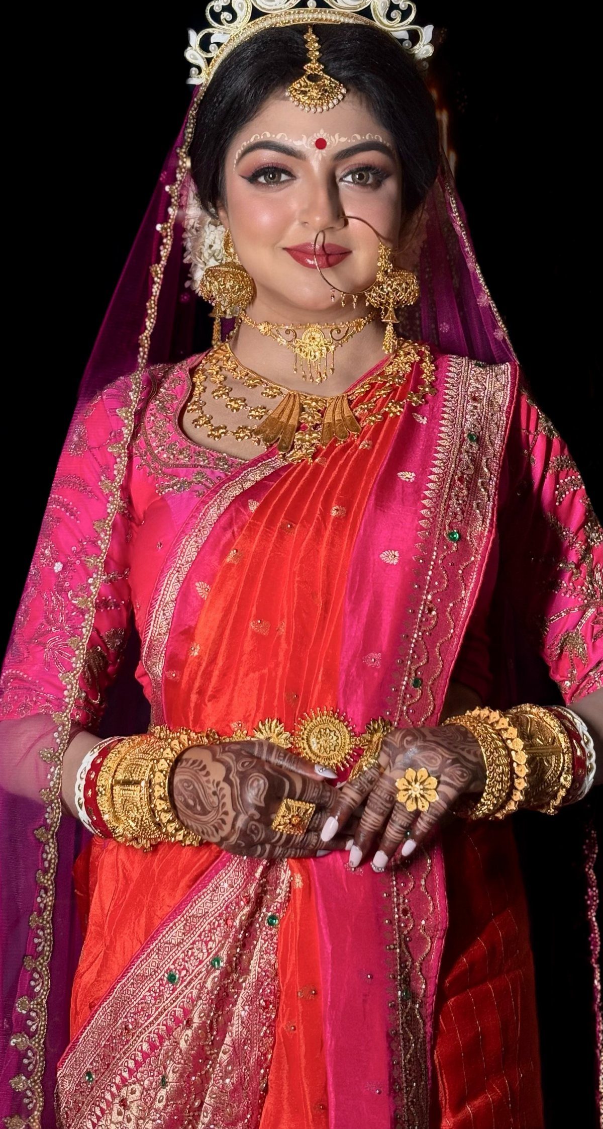 Indian bride wearing a red bindi, gold jewelry, and a pink embroidered saree