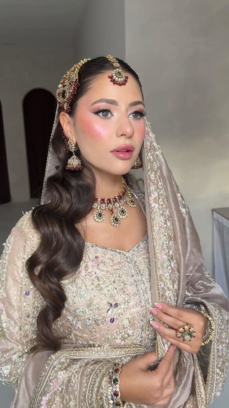 Woman in beige bridal lehenga with soft glam makeup and gold jewelry