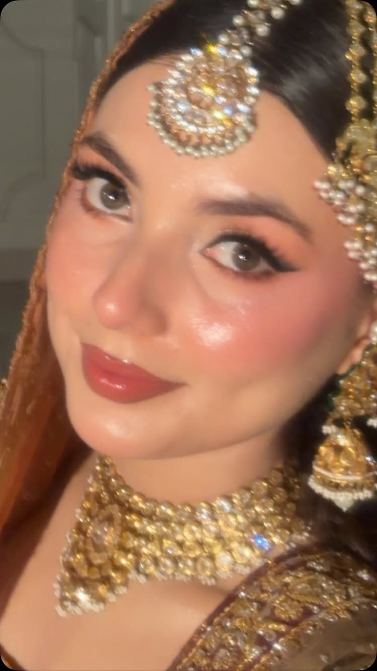 Woman with bridal makeup featuring winged eyeliner and heavy gold traditional jewelry