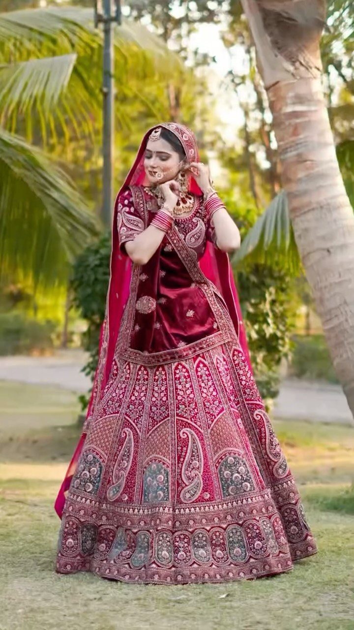Bride in magenta velvet lehenga posing in a garden with palm trees