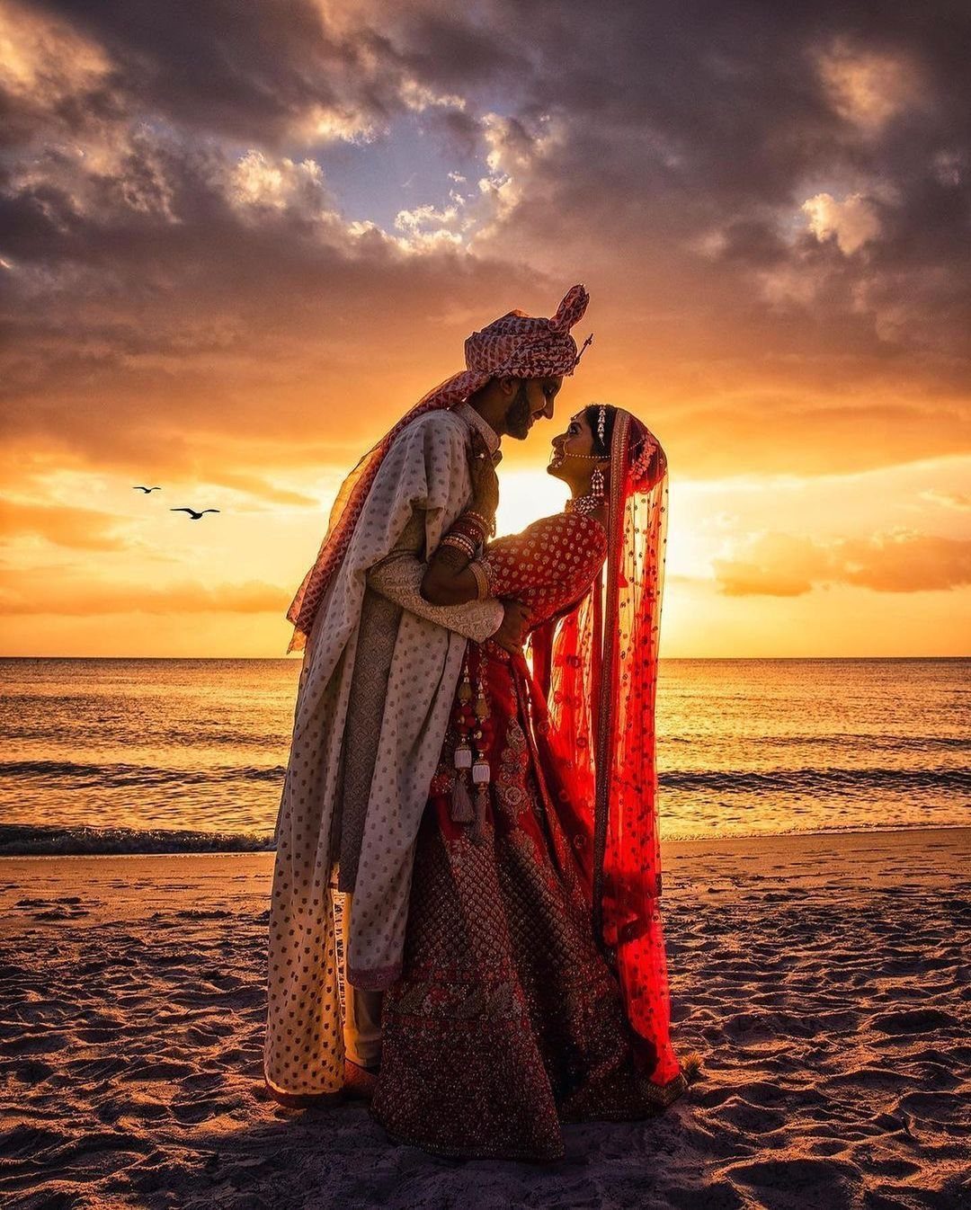 Indian wedding couple embracing on a beach during a golden sunset.