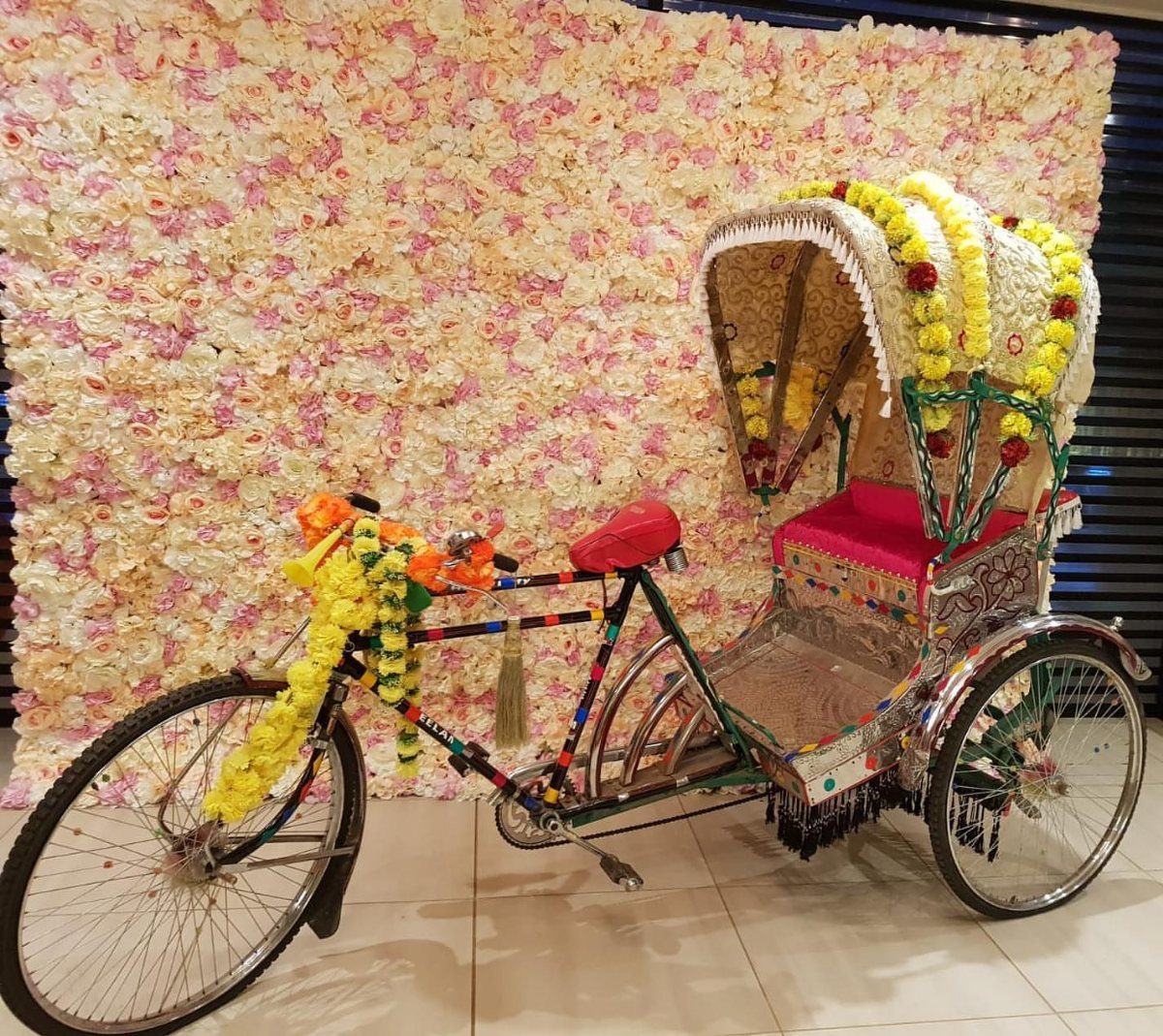 Decorated cycle rickshaw with floral garlands against a pink and white flower wall
