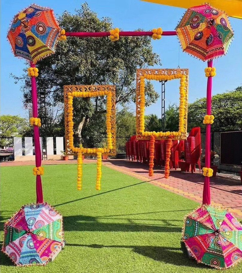 Colorful photo booth setup with embroidered umbrellas and yellow marigold floral frames outdoors.