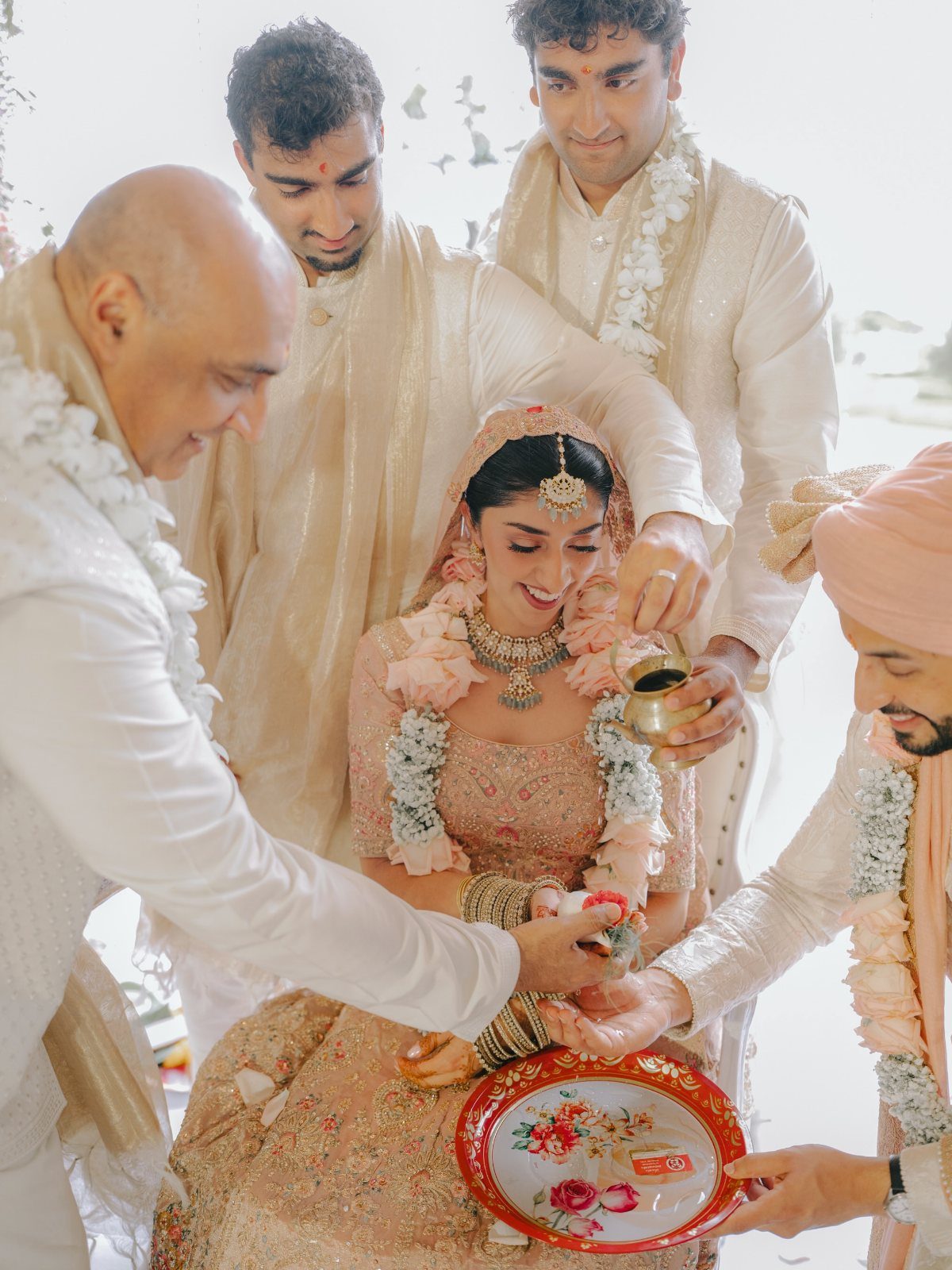 Bride in peach lehenga participating in a wedding ritual with men in white attire