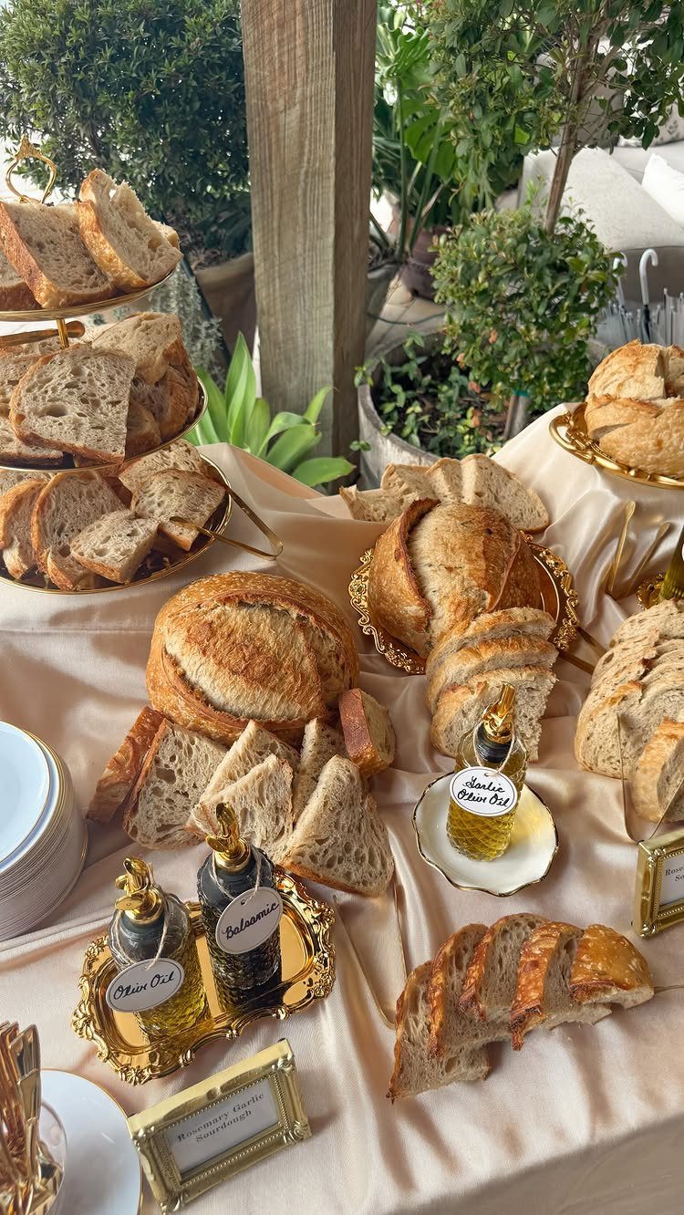 Assorted artisanal breads and dipping oils displayed on a beige cloth with gold platters.