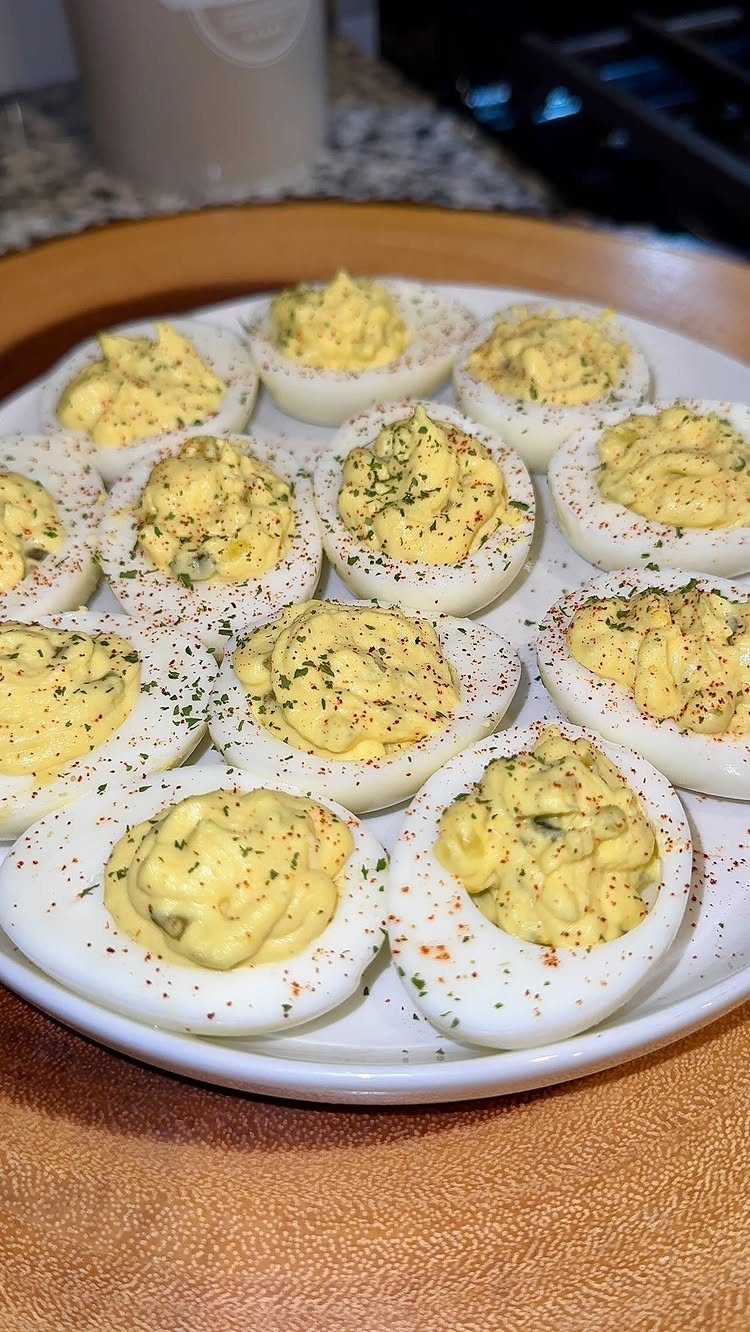 Deviled eggs on a white plate garnished with paprika and fresh green herbs.