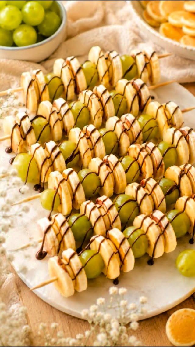 Fruit skewers with bananas and green grapes drizzled with chocolate on marble platter